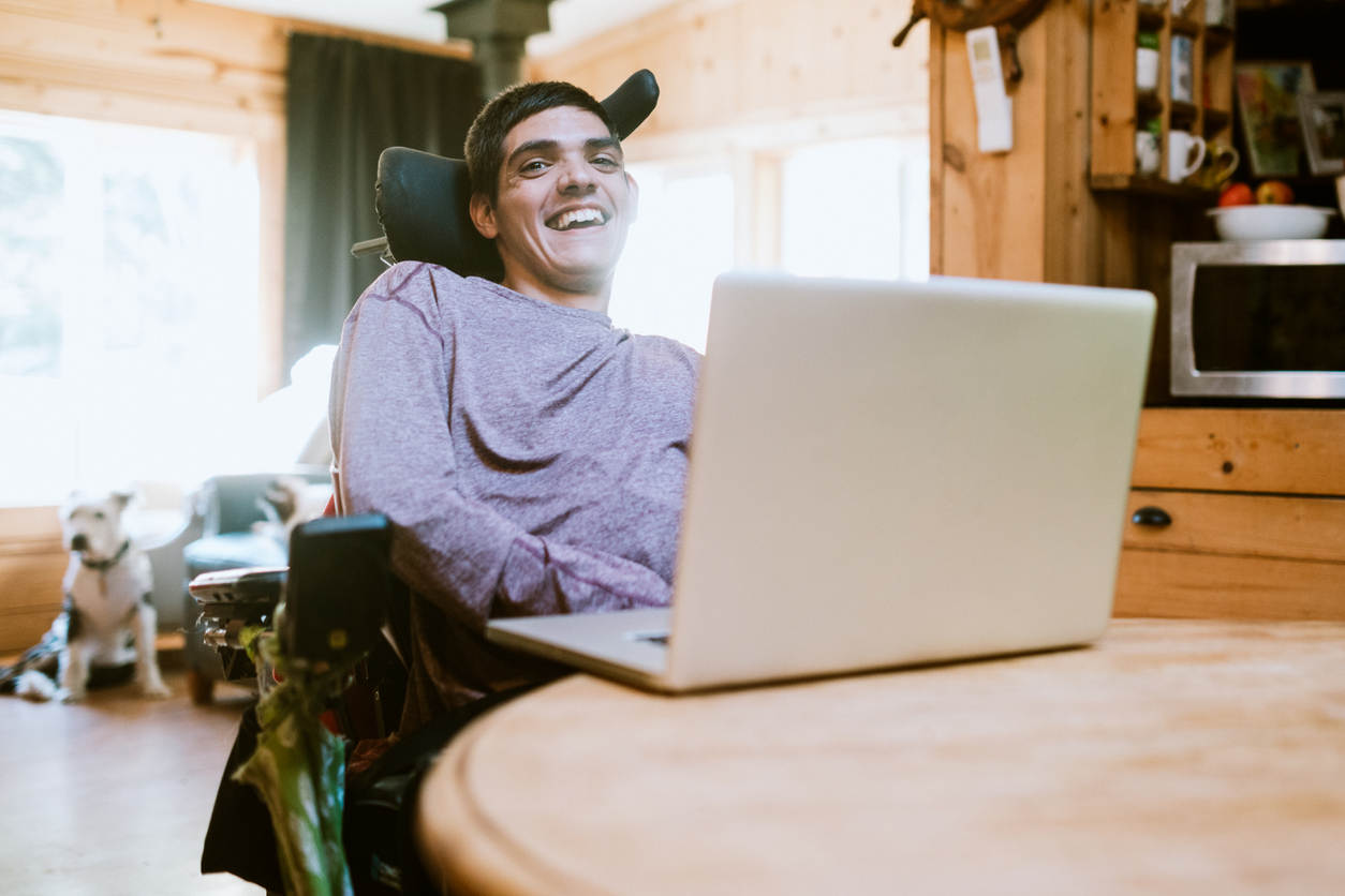 Image of man with disability in a wheelchair with a laptop open in front of him.